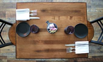 a wooden dining table set with plates , bowls , cups , and utensils , ready for a meal at Plum Point Lodge