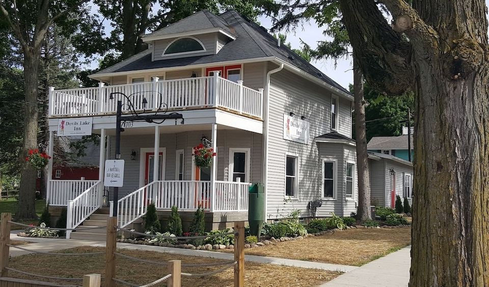 a two - story house with a white picket fence and large windows , surrounded by trees and grass at Devils Lake Inn