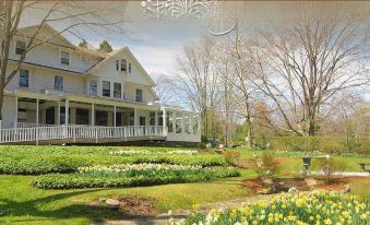 a large white house surrounded by a lush green garden , with various flowers and plants in the yard at Copper Beech Inn