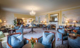 a cozy living room with blue couches , chairs , and a fireplace , decorated with flowers and paintings on the walls at The Inn at Dromoland