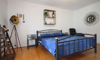 a modern bedroom with wooden flooring , white walls , and a blue bedspread , accompanied by various items such as a lamp , speaker , and at Lolita