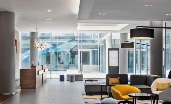 a modern hotel lobby with comfortable seating , a yellow chair , and large windows offering views of the surrounding area at Courtyard Munich Garching