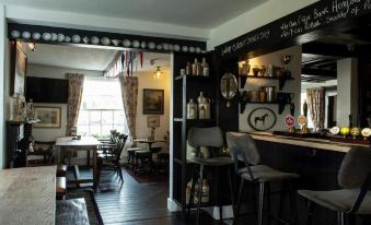 a bar with a black counter and stools , surrounded by wooden tables and chairs , and shelves filled with bottles at The Carden Arms