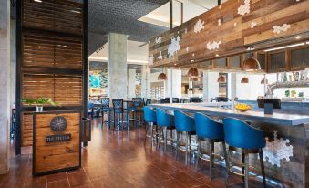 a modern restaurant with wooden floors , blue chairs , and wooden tables , as well as a bar area at The Stella Hotel, Autograph Collection