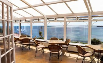 a modern , open - air restaurant with large windows offering views of the sea and mountains , featuring wooden tables and chairs at Grand Hotel Swanage