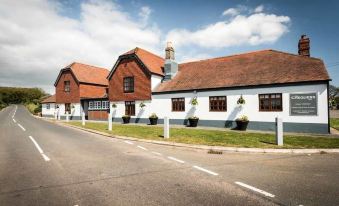 a street view of a two - story building with a red roof and white walls , surrounded by green grass and blue skies at The Chequers Inn