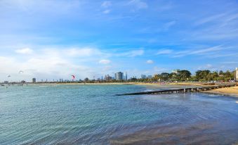 a beach scene with a wooden pier extending into the water , surrounded by a city skyline in the background at Middle Park Hotel