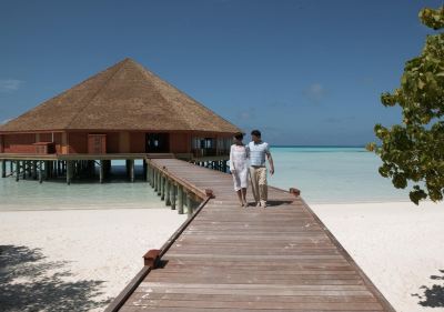 a man and a woman are walking hand in hand on a wooden pier , overlooking the ocean at Vilamendhoo Island Resort & Spa