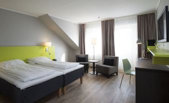 a hotel room with a large bed , two chairs , and a desk , all set against a backdrop of windows at Thon Hotel Hallingdal