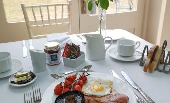a breakfast table set with a variety of food items , including eggs , sausage , bacon , and a vase of flowers at Cleatham Hall
