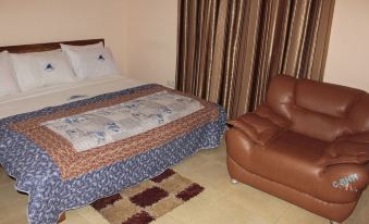 a bed with a floral comforter and pillows is next to a brown leather armchair in a room with curtains at Blue Hill Hotel