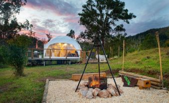 a tent is set up in a field with a fire pit and a hot tub nearby at Nature Domes