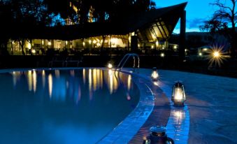 a nighttime view of a swimming pool and surrounding area , with lights illuminating the water and reflecting the lights of the buildings in the background at Ashnil Samburu Camp