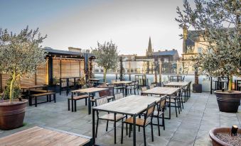 a rooftop restaurant with wooden tables and chairs , surrounded by trees and a view of the city at Mercure Newport