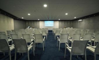 a large conference room with rows of white chairs arranged in a semicircle , and a projector screen mounted on the wall at Hotel Capital