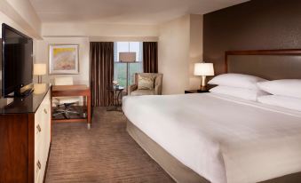 a large bed with white sheets is in a room with a desk , chair , and lamp at Hyatt Regency Long Island