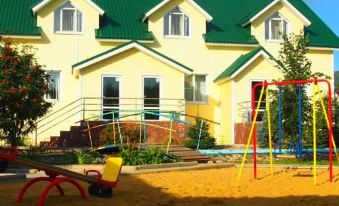 a yellow house with a green roof , surrounded by a sandy play area with swings and a slide at Elizaveta