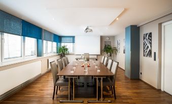 a conference room with a long wooden table , chairs , and plants , set for a meeting or presentation at Leonardo Hotel Berlin