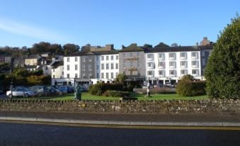 a large white building with a sloping roof and multiple balconies , surrounded by trees and grass at Actons Hotel Kinsale