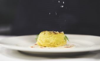 a white plate with a small , yellow vegetable dish on it , garnished with herbs and drizzled with sauce at Hotel Mondole