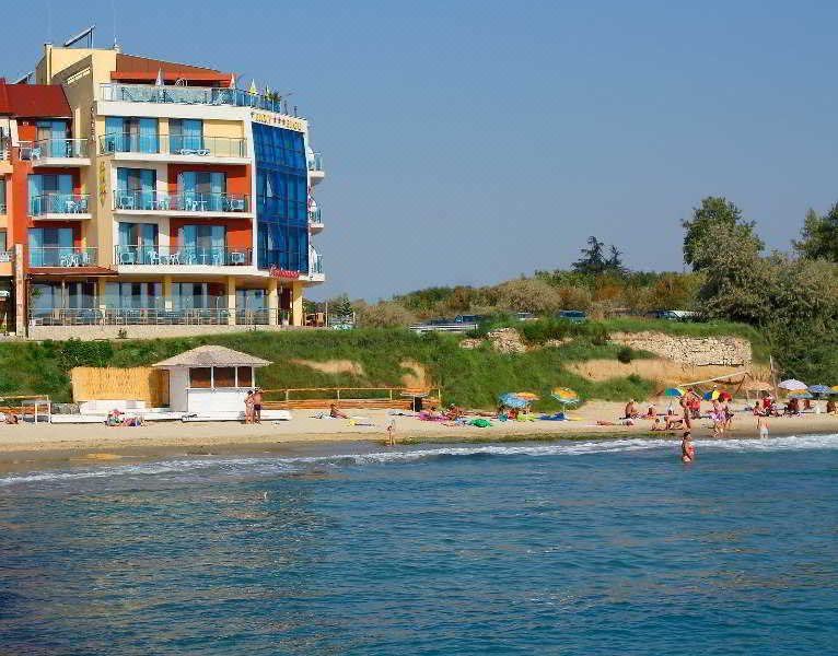 a beach with a building in the background and people swimming in the water near the shore at Hotel Bijou