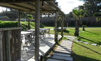 an outdoor dining area with a wooden pergola and tables , surrounded by grass and palm trees at Punta del Este Arenas Hotel