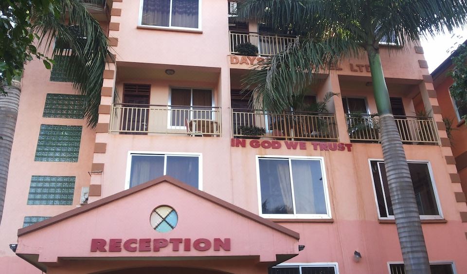 "a pink building with the words "" in god we trust "" written on it , surrounded by palm trees and other greenery" at DaysInn Hotel