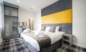 a large bed with a yellow and black headboard is in a room with gray carpet at 42 Apart-Hotel
