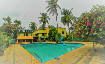 a large swimming pool with palm trees and a building in the background , surrounded by palm trees at Hotel Sangam