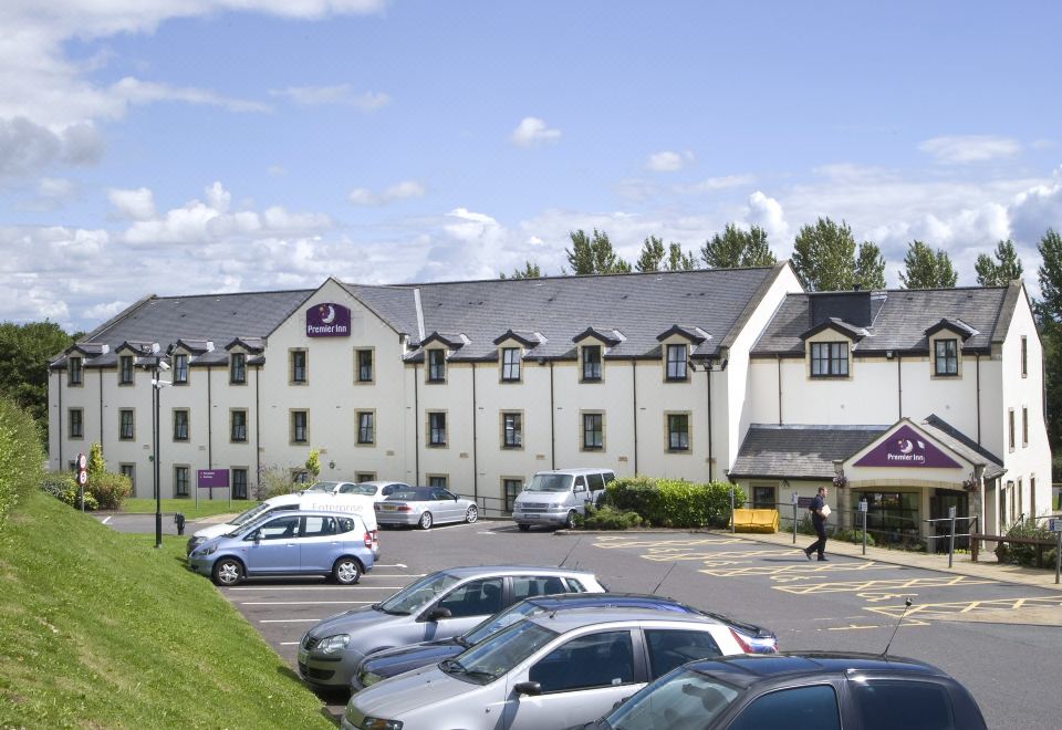 a large hotel with a parking lot filled with cars , under a clear blue sky at Premier Inn Glasgow (Milngavie)