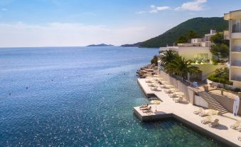 a beach scene with a dock and lounge chairs overlooking the ocean , surrounded by palm trees at Aminess Lume Hotel