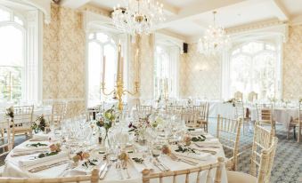 a formal dining room with a round table set for a wedding reception , surrounded by chairs and adorned with flowers at Rowton Castle