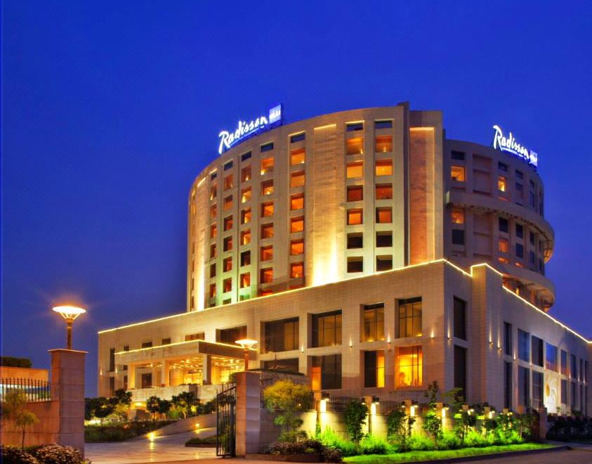 a large hotel building lit up at night , surrounded by trees and a fountain in front of it at Radisson Blu New Delhi Dwarka