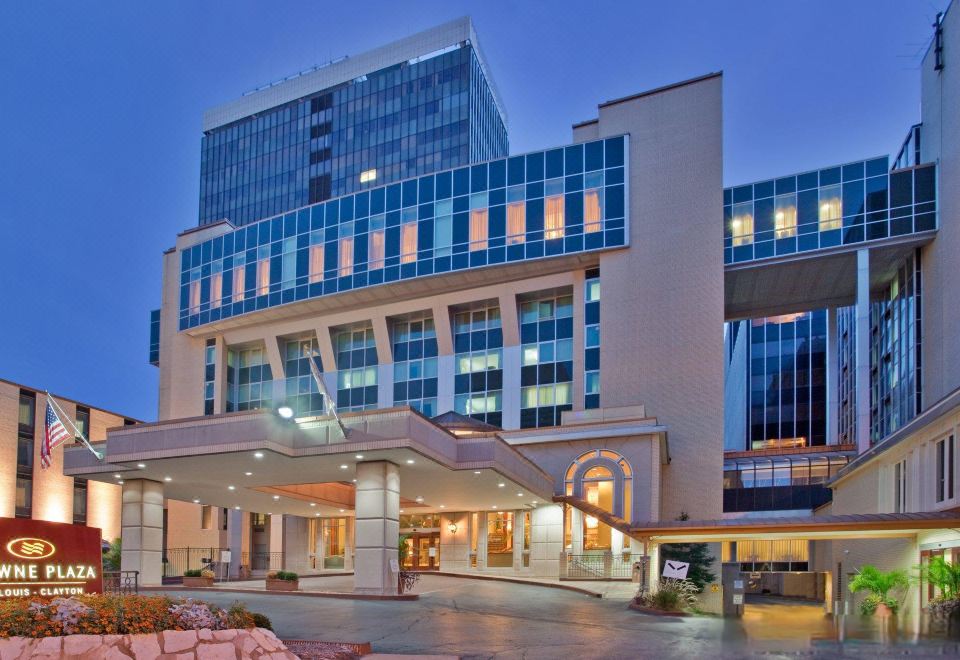 a large , modern building with a curved entrance and glass windows is lit up at night at Clayton Plaza Hotel & Extended Stay