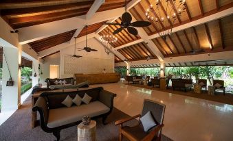 a large room with a high ceiling and wooden beams , featuring a black couch , chairs , and a coffee table at The Residence Maldives at Dhigurah