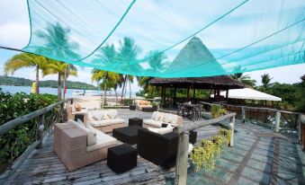a wooden deck with a variety of seating options , including couches , chairs , and a dining table at Badian Island Wellness Resort