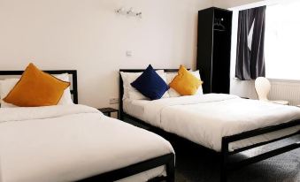 a hotel room with two beds , each equipped with white linens and colorful pillows , along with black nightstands and a window at Wanstead Hotel