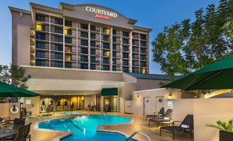 a large hotel with a swimming pool and outdoor seating area , surrounded by trees and a clear blue sky at Courtyard by Marriott Los Angeles Pasadena/Monrovia