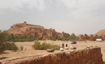 a group of people standing on a dirt road near a rocky hill , with a castle in the background at Bagdad Cafe