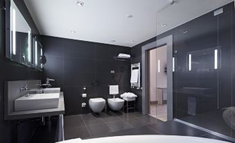 a modern bathroom with a black and white color scheme features two toilets , a sink , and a toilet paper roll at NH Parma