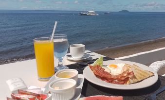 a table with a breakfast spread , including fruit and pastries , overlooking the ocean and a ferry at Sierra Resort
