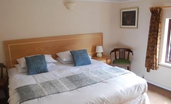 a large bed with a wooden headboard and two blue pillows is in a room with a chair , lamp , and framed picture on the wall at Derby Inn