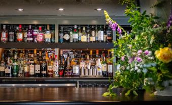 a bar with a variety of bottles and wine glasses , as well as a vase of flowers on the counter at The Cricketers Clavering