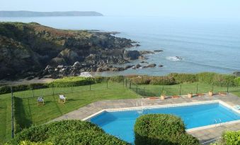 a large swimming pool is surrounded by lush greenery and overlooks the ocean , with a view of rocky shoreline in the distance at Watersmeet Hotel