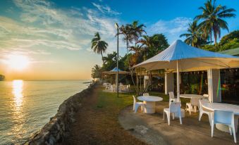 a beautiful outdoor setting with umbrellas , tables , and chairs set up near the ocean , creating a relaxing atmosphere at Madang Resort