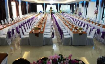 a long banquet hall with rows of tables and chairs , purple tablecloths , and flowers in the center at Thaiasia Goldensea Resort
