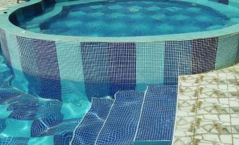 a swimming pool with blue and white tiles , surrounded by a wooden deck and stairs at Alfa Hotel