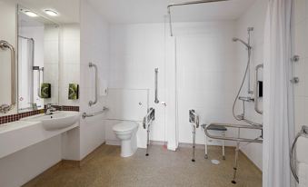 a bathroom with a toilet , sink , and shower area , as well as a shower with a handrail at Premier Inn Honiton