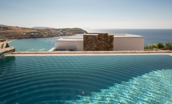 a large outdoor swimming pool surrounded by a building , with the ocean visible in the background at The Summit of Mykonos