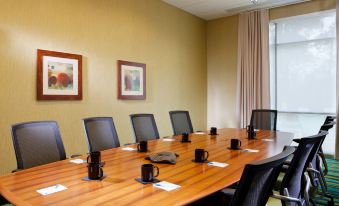 a wooden conference table with chairs , cups , and a window in the background , surrounded by framed pictures on the walls at SpringHill Suites Houston the Woodlands